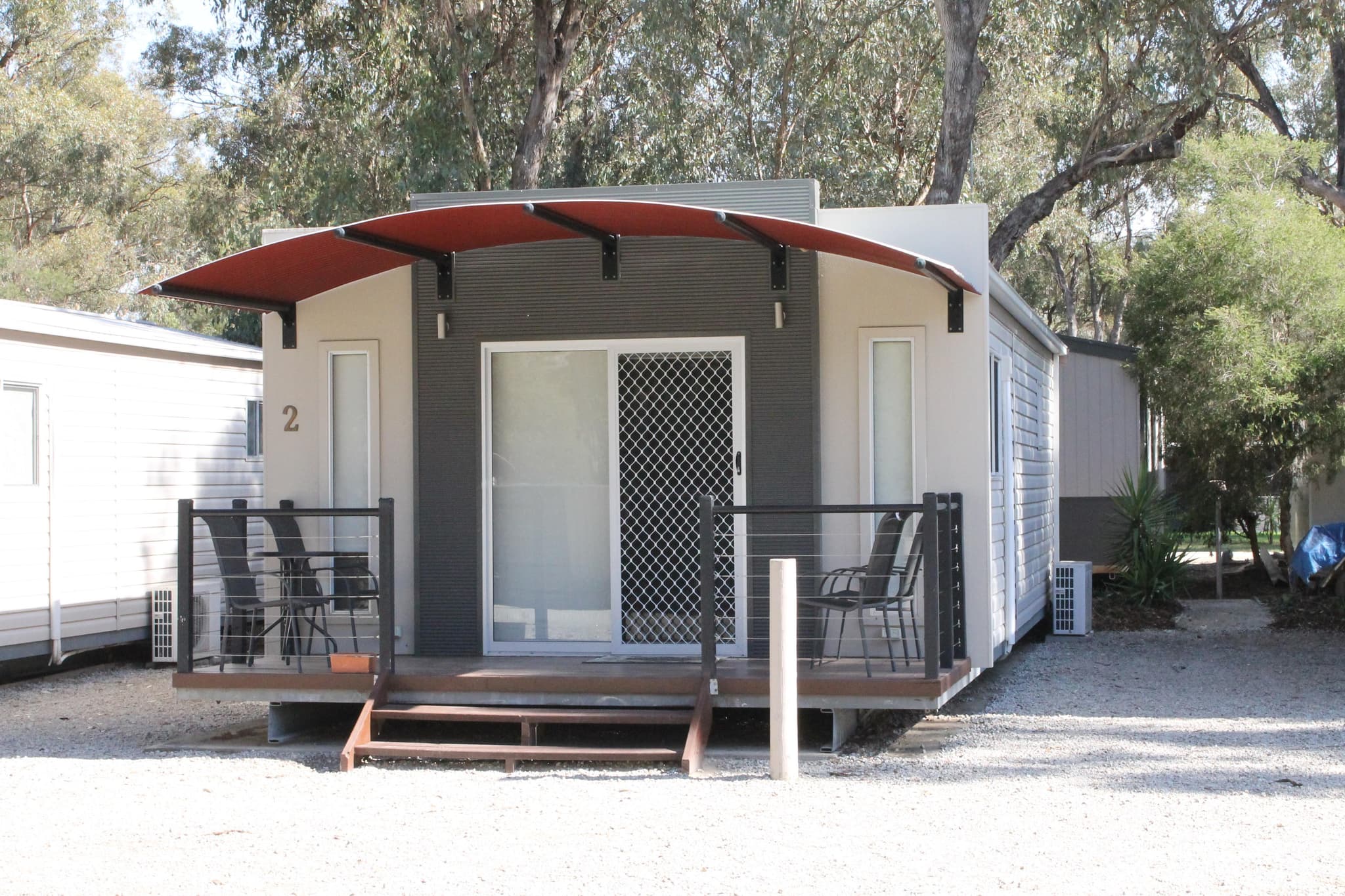 Cabin 2 with curved red awning and timber deck at Torrumbarry Weir Holiday Park, Patho VIC, set among gum trees