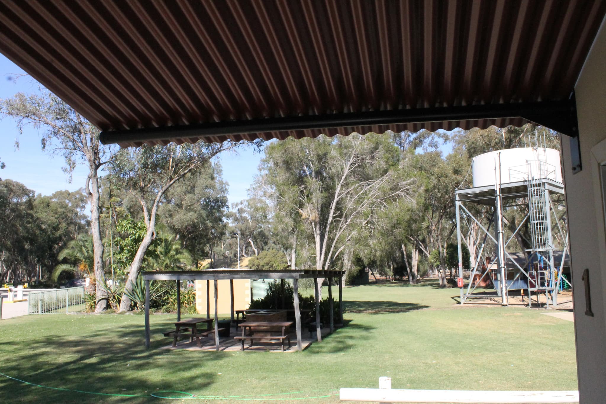 View from the Fleetwood Rainbow Cabin veranda across the lawn to a picnic shelter and water tower at Torrumbarry Weir Holiday Park