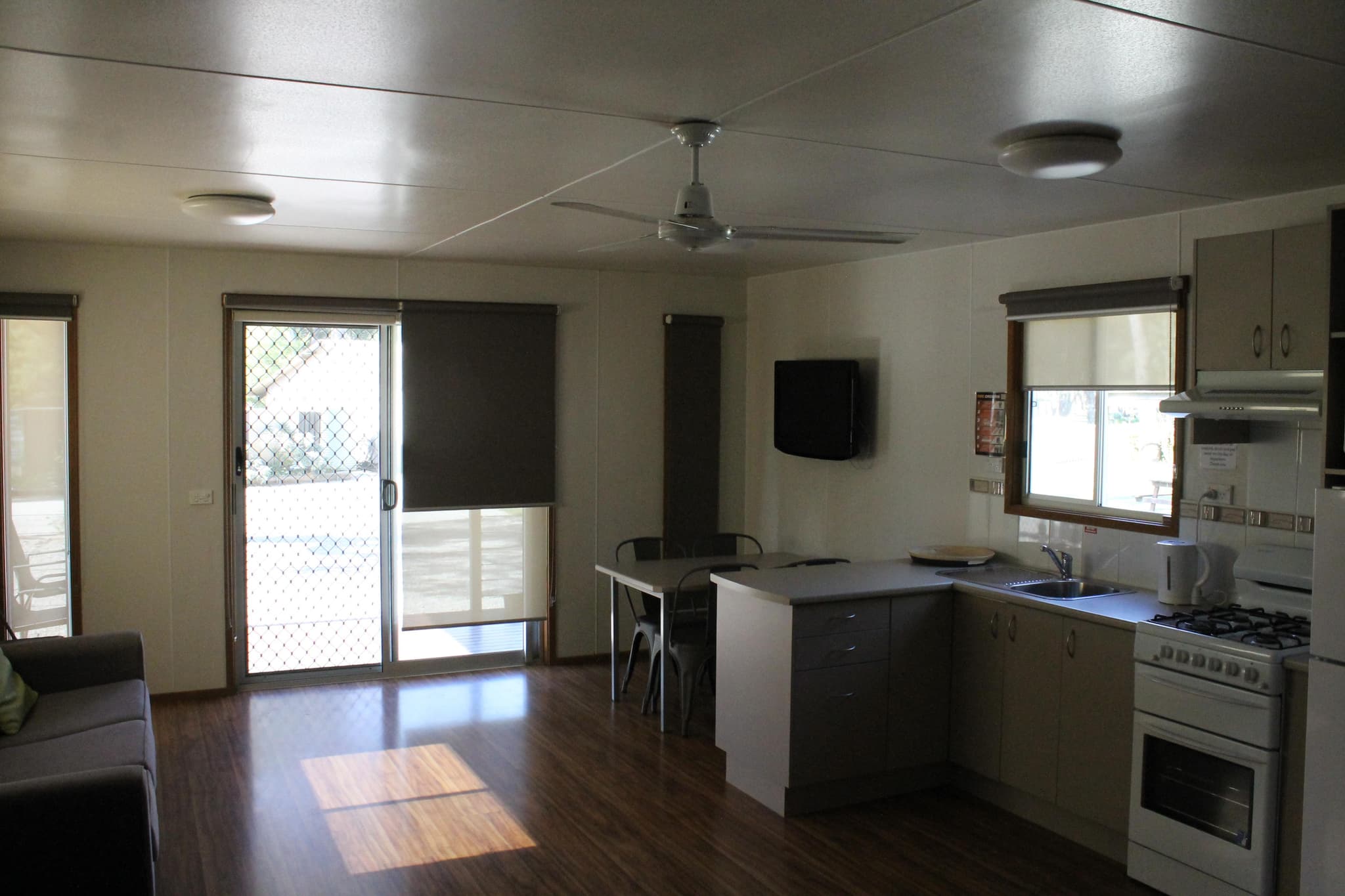 Open plan kitchen and living area in a Fleetwood Rainbow Cabin at Torrumbarry Weir Holiday Park, with dining table, wall mounted TV and timber flooring