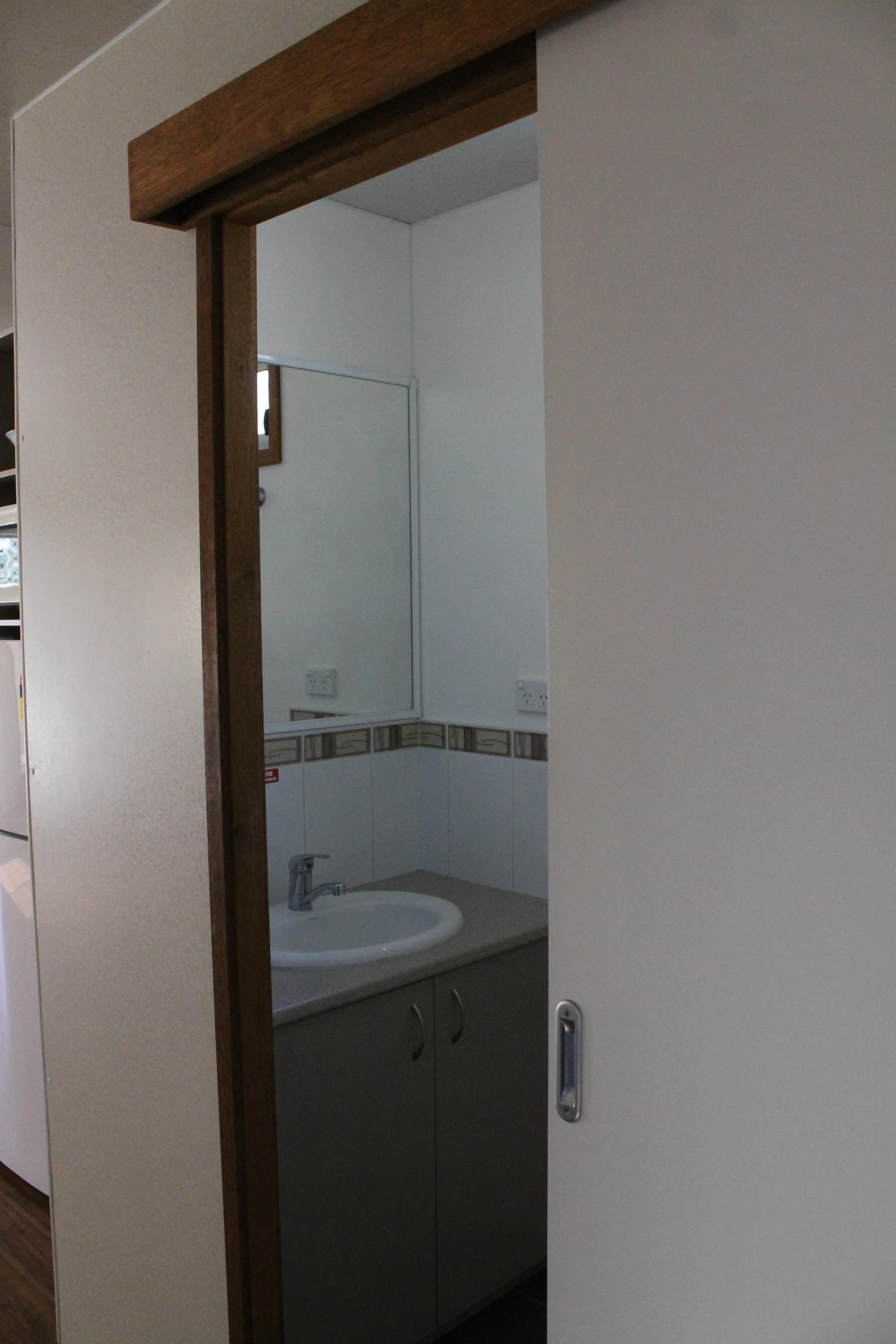 Sliding door opens to the ensuite bathroom of the Fleetwood Rainbow Cabin at Torrumbarry Weir Holiday Park, with vanity, mirror and sink