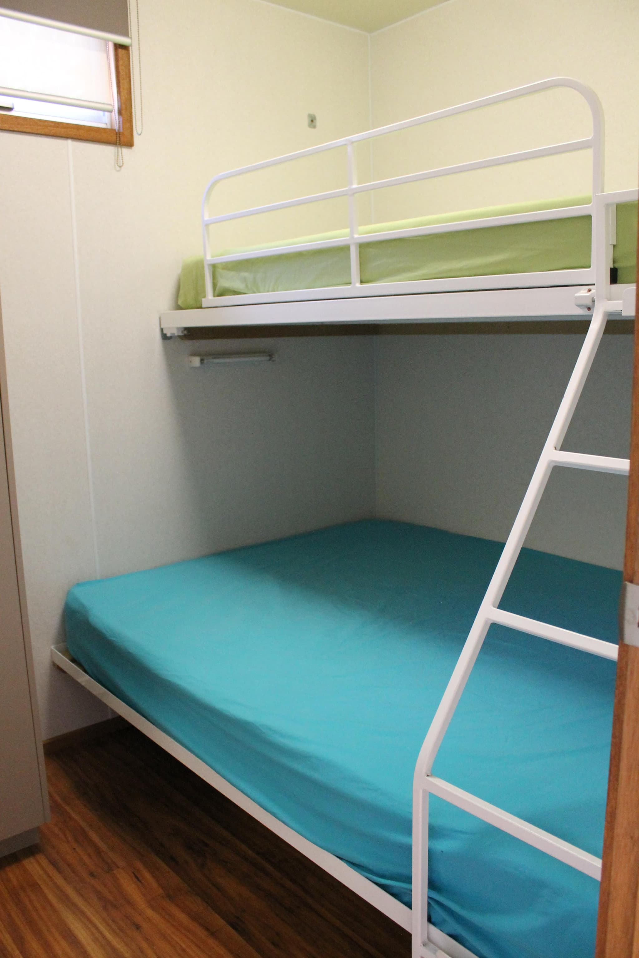 White bunk bed with teal lower mattress and green top bunk in a Fleetwood Rainbow Cabin at Torrumbarry Weir Holiday Park
