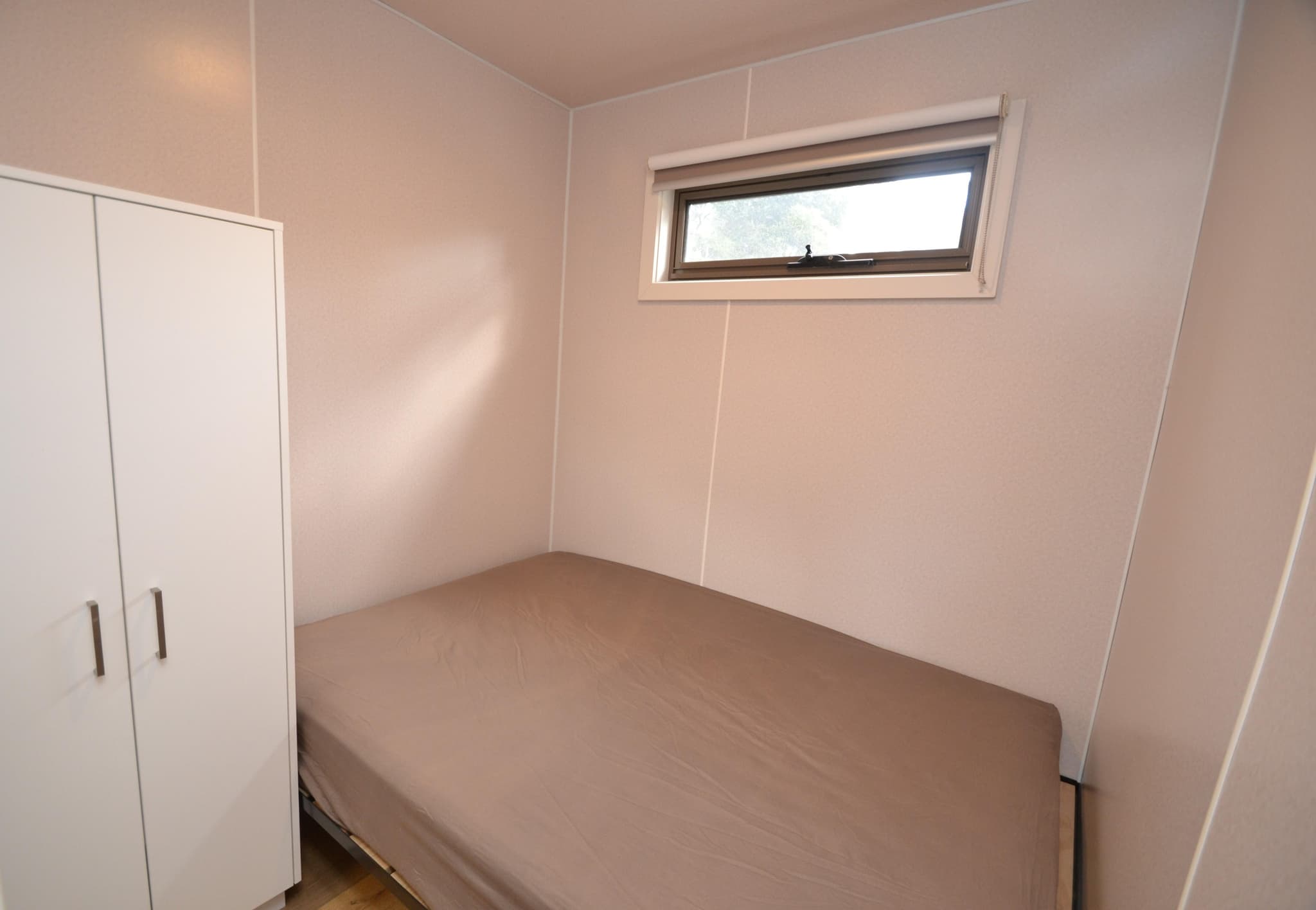 Single bedroom in a Deluxe Riverview Cabin at Torrumbarry Weir Holiday Park, with a made-up bed and white built-in wardrobe