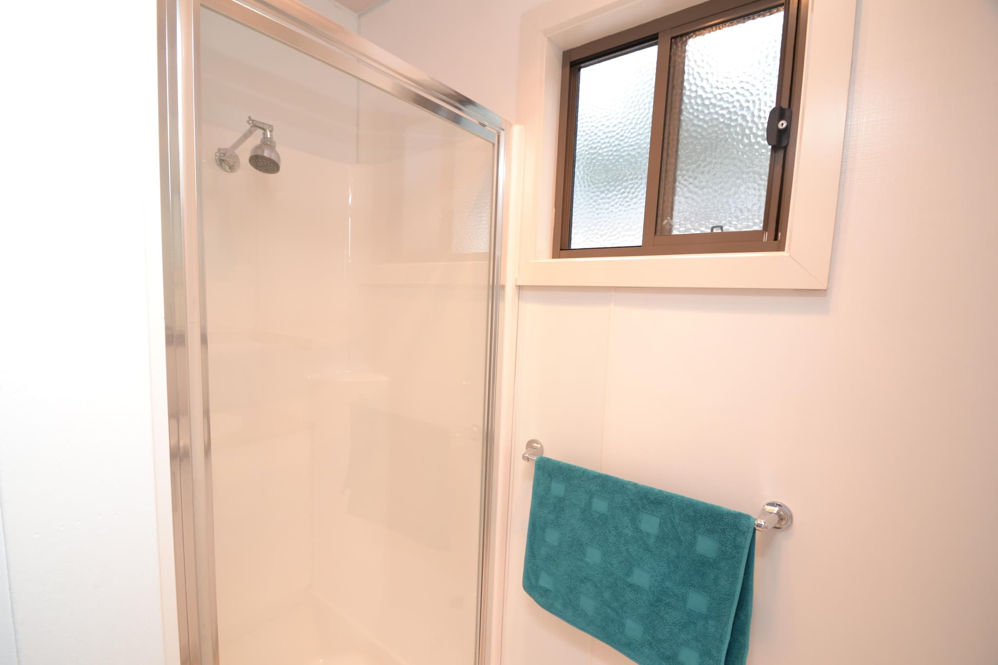 Ensuite bathroom in a Deluxe Riverview Cabin at Torrumbarry Weir Holiday Park, showing glass shower screen, chrome showerhead and teal towel