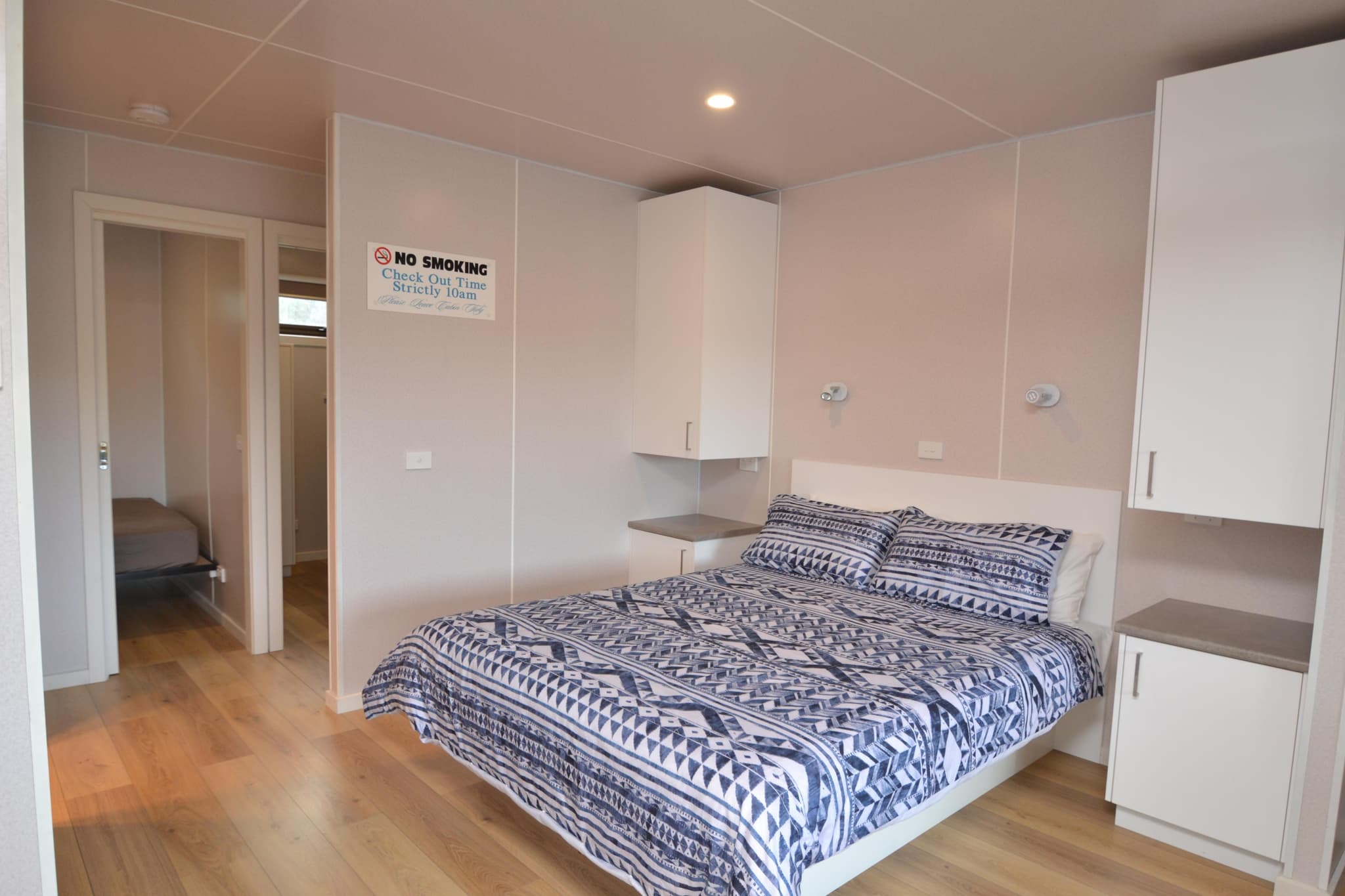 Cabin bedroom with navy geometric-patterned bedding on a queen bed, white cabinetry and timber floors at Torrumbarry Weir Holiday Park