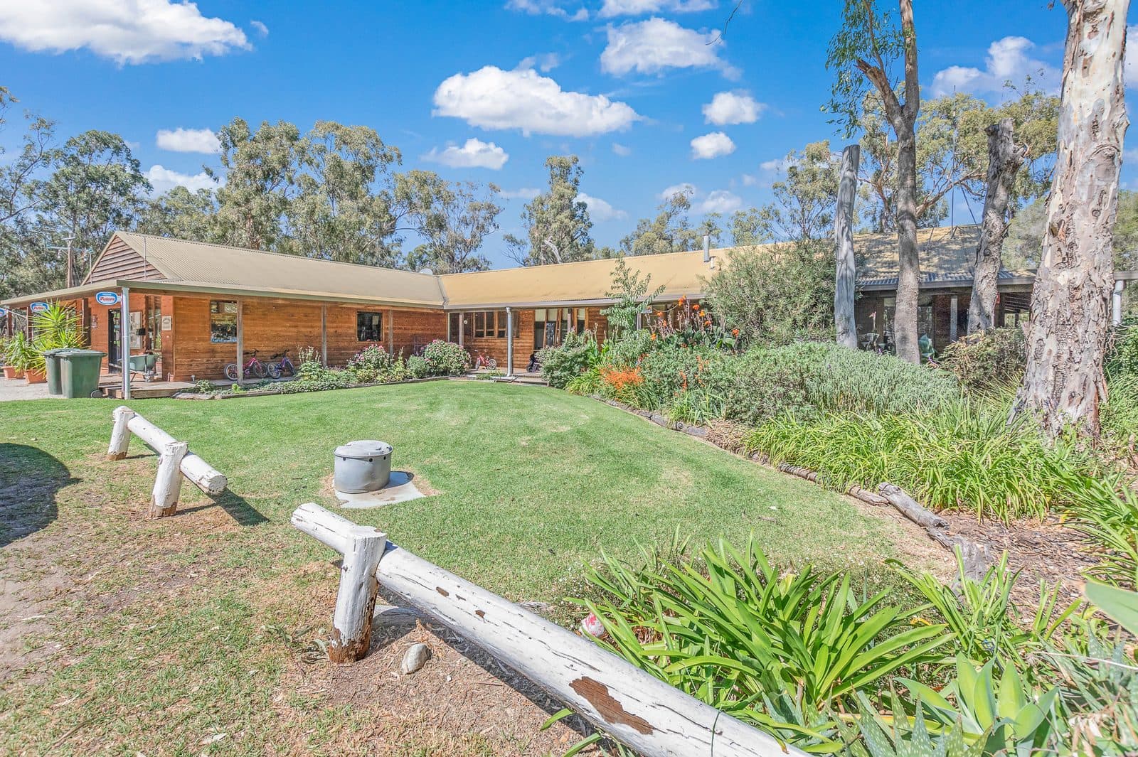 Grassed lawn with white timber guard rail in front of the wooden park building at Torrumbarry Weir Holiday Park, Patho VIC