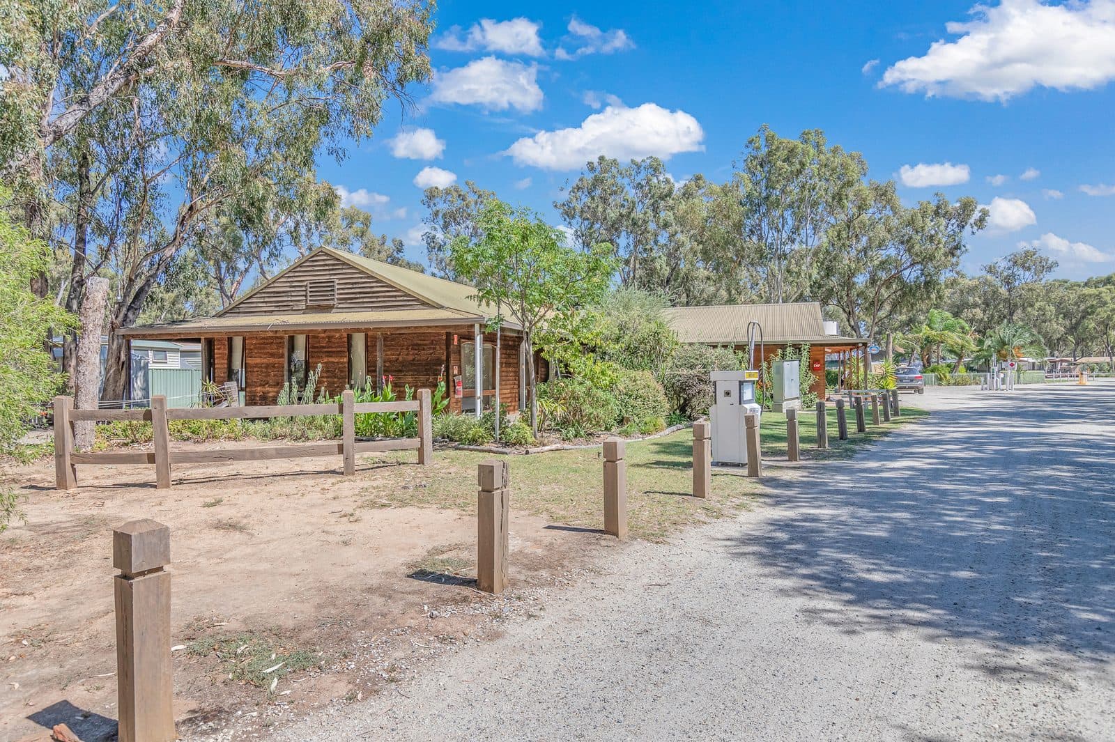 Timber park building with veranda beside gravel driveway at Torrumbarry Weir Holiday Park, Patho VIC, shaded by gum trees