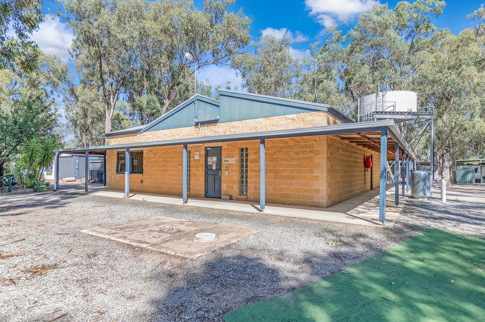 Brick amenities block with wide veranda and Gents entrance at Torrumbarry Weir Holiday Park, shaded by gum trees